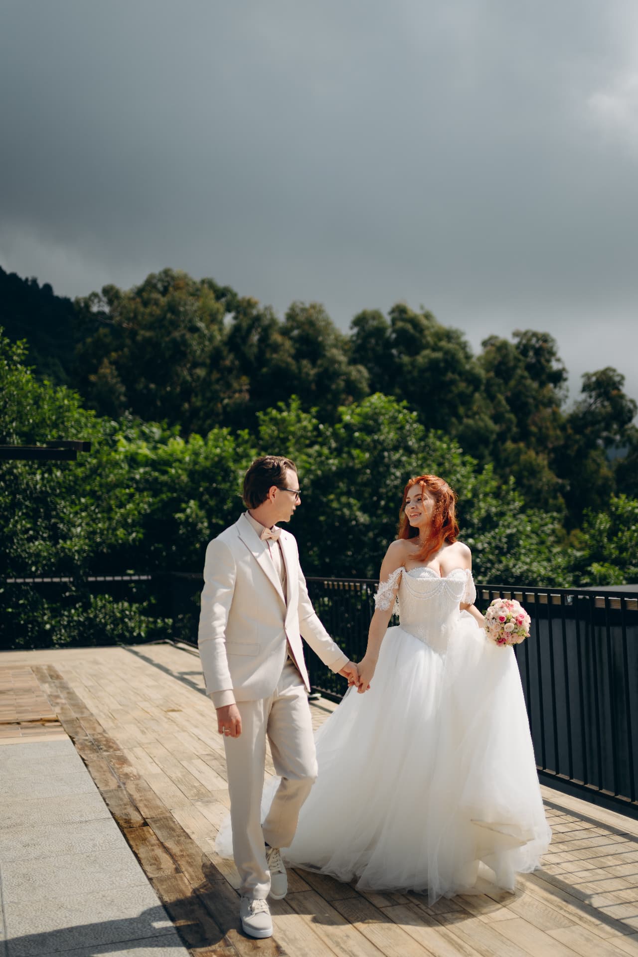 Couple walking hand in hand on a wooden terrace with forest and dramatic sky behind