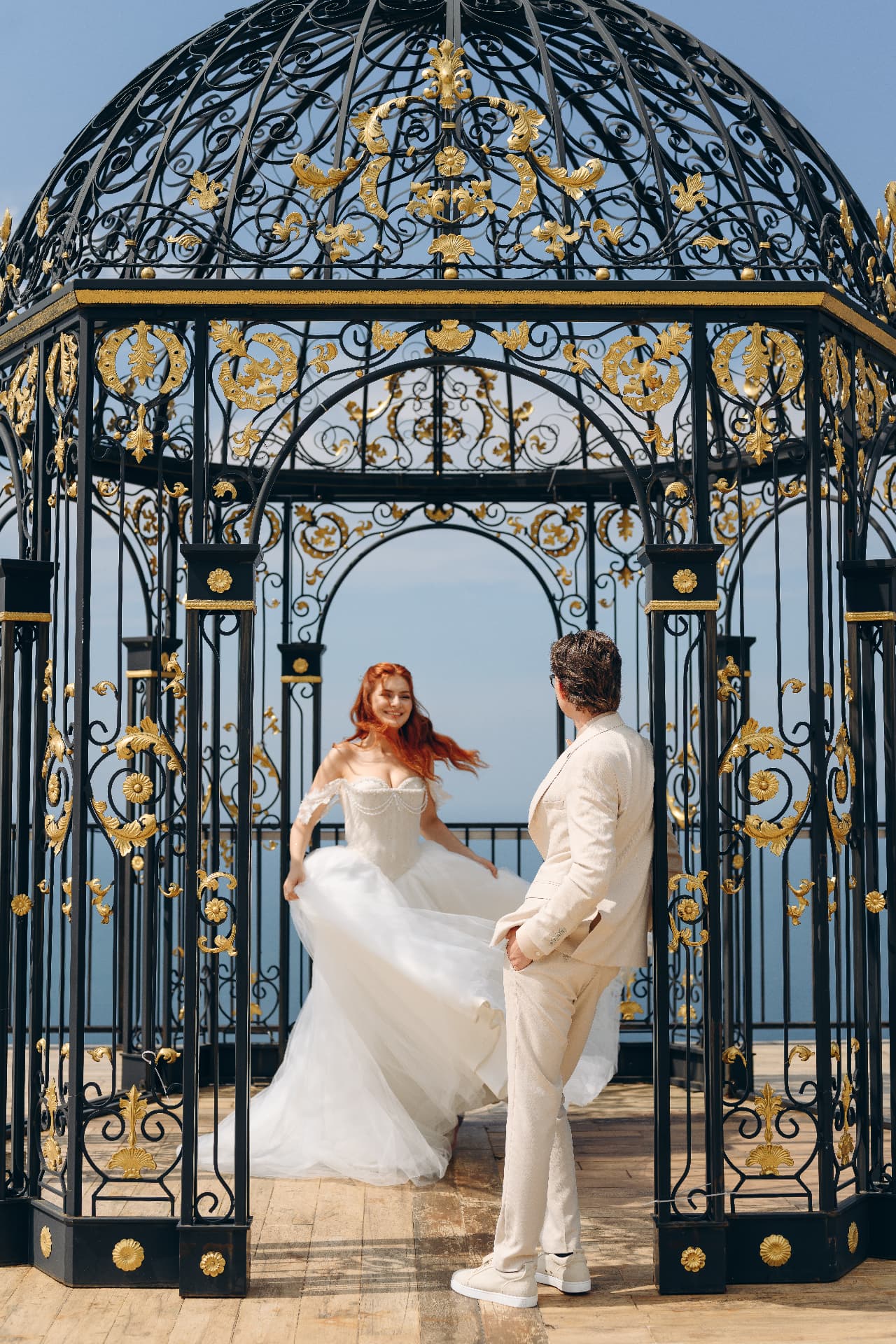 Bride twirling her gown beneath a gilded wrought-iron gazebo overlooking the sea
