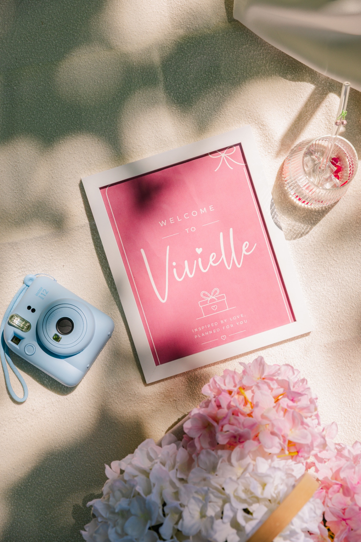 Flatlay with pastel instax camera, Vivielle welcome print and hydrangea florals — Vivielle Events Budapest