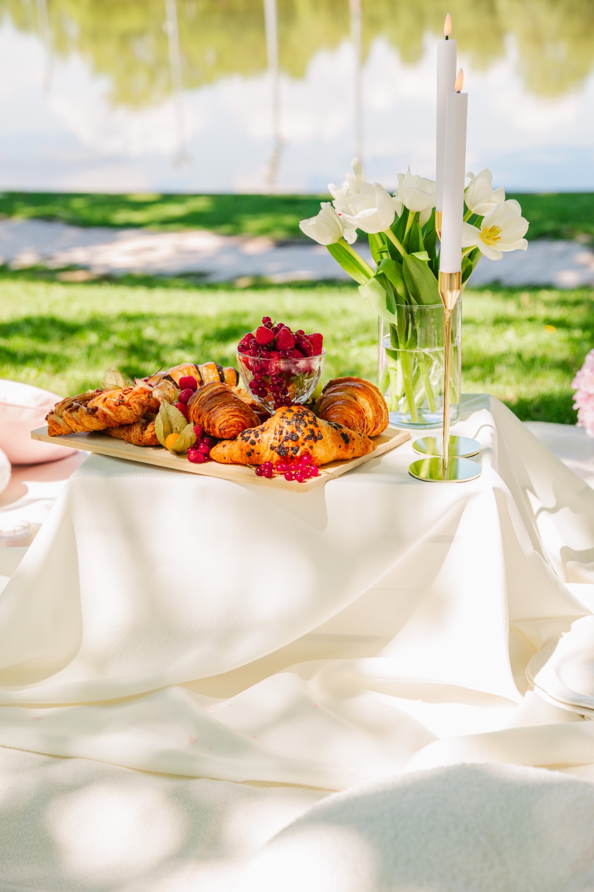 Lakeside picnic tablescape with artisan croissants, berries, white tulips and taper candles — Vivielle Events Budapest
