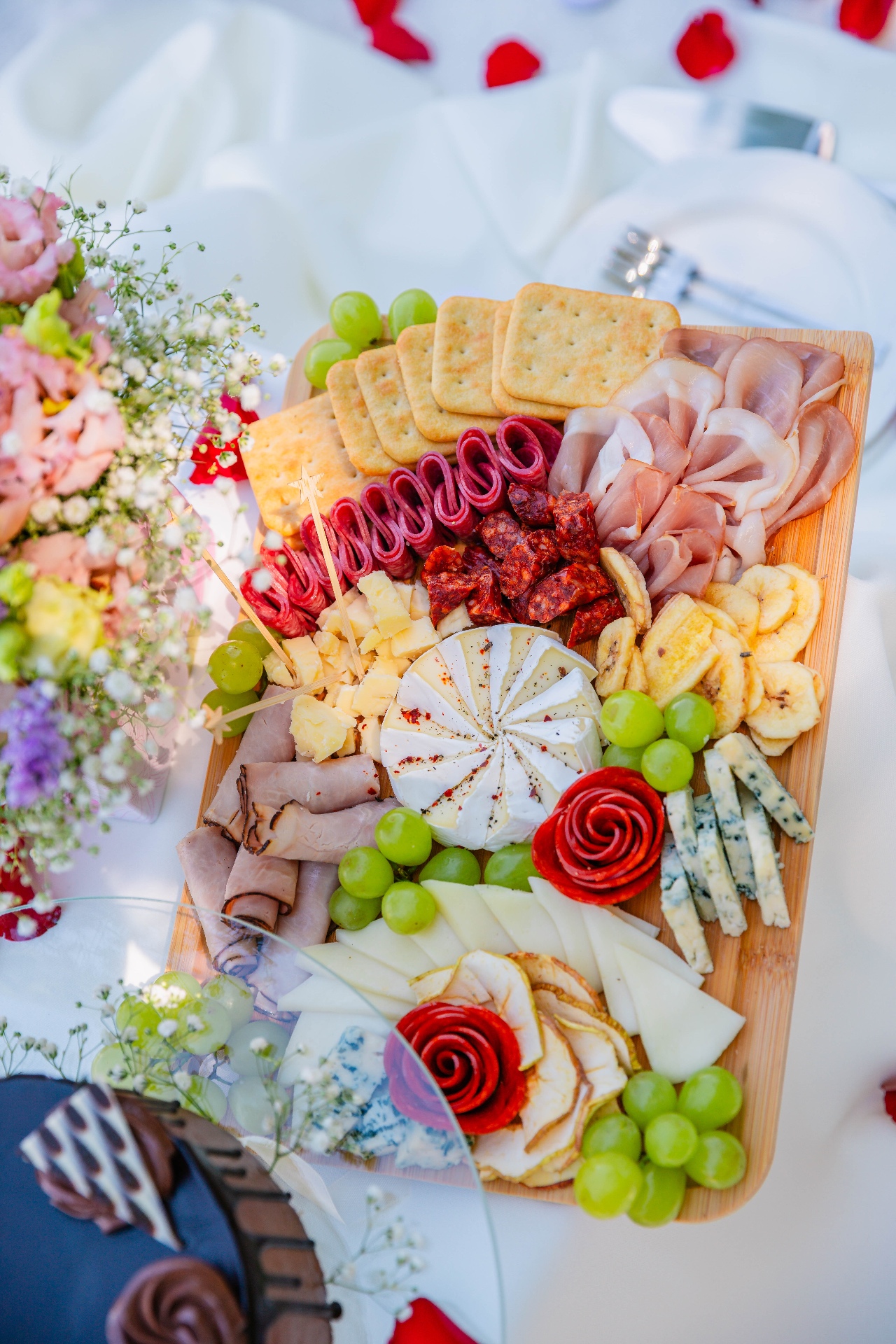 Gourmet charcuterie board with brie, prosciutto, salami roses, grapes and pastel florals — luxury picnic Budapest by Vivielle Events
