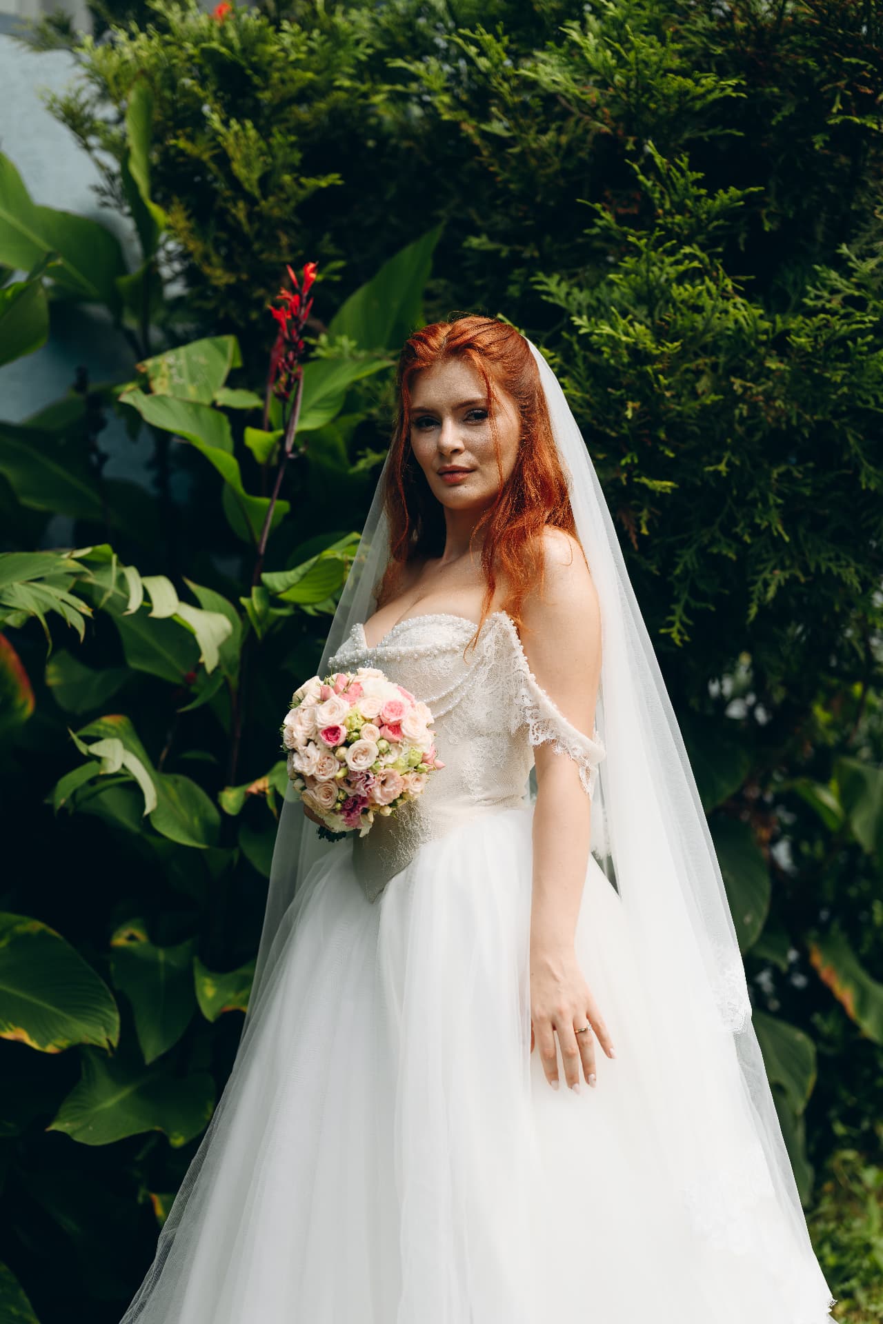 Bridal portrait among lush tropical greenery with a pink and ivory bouquet