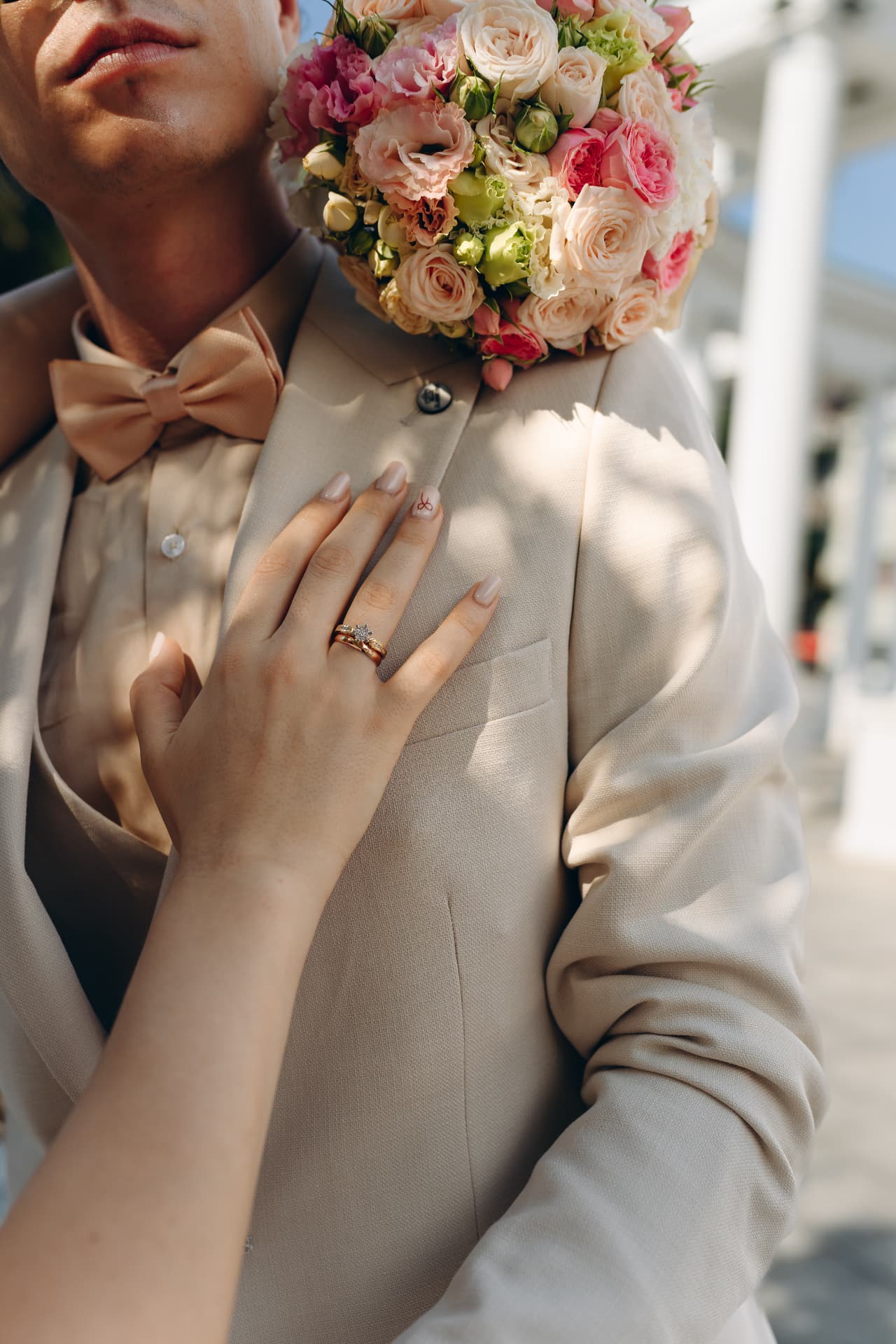 Close-up of bride's hand with wedding rings resting on her groom's cream jacket beside the bouquet