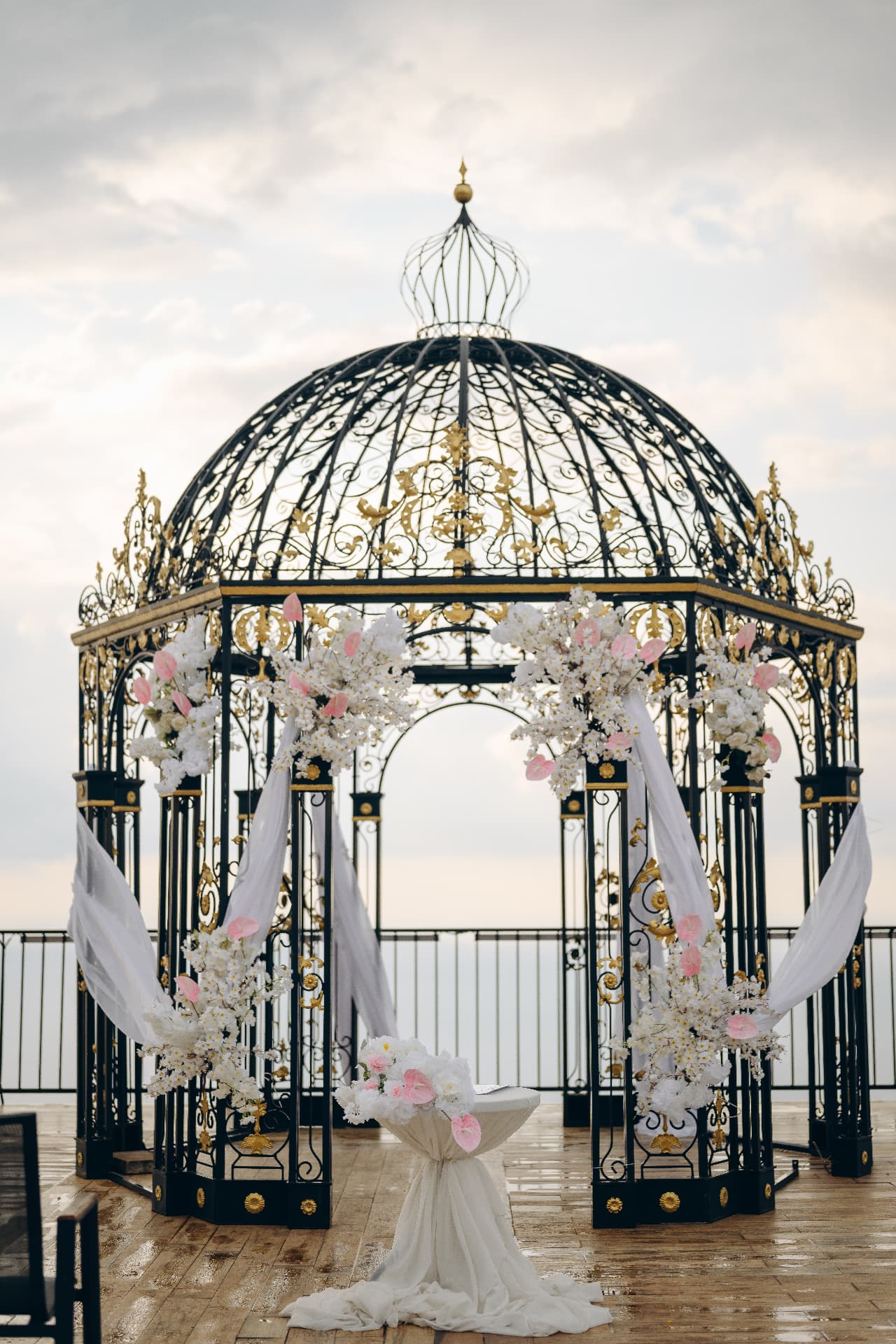 White and blush floral wedding ceremony styling on an ornate black and gold seaside gazebo