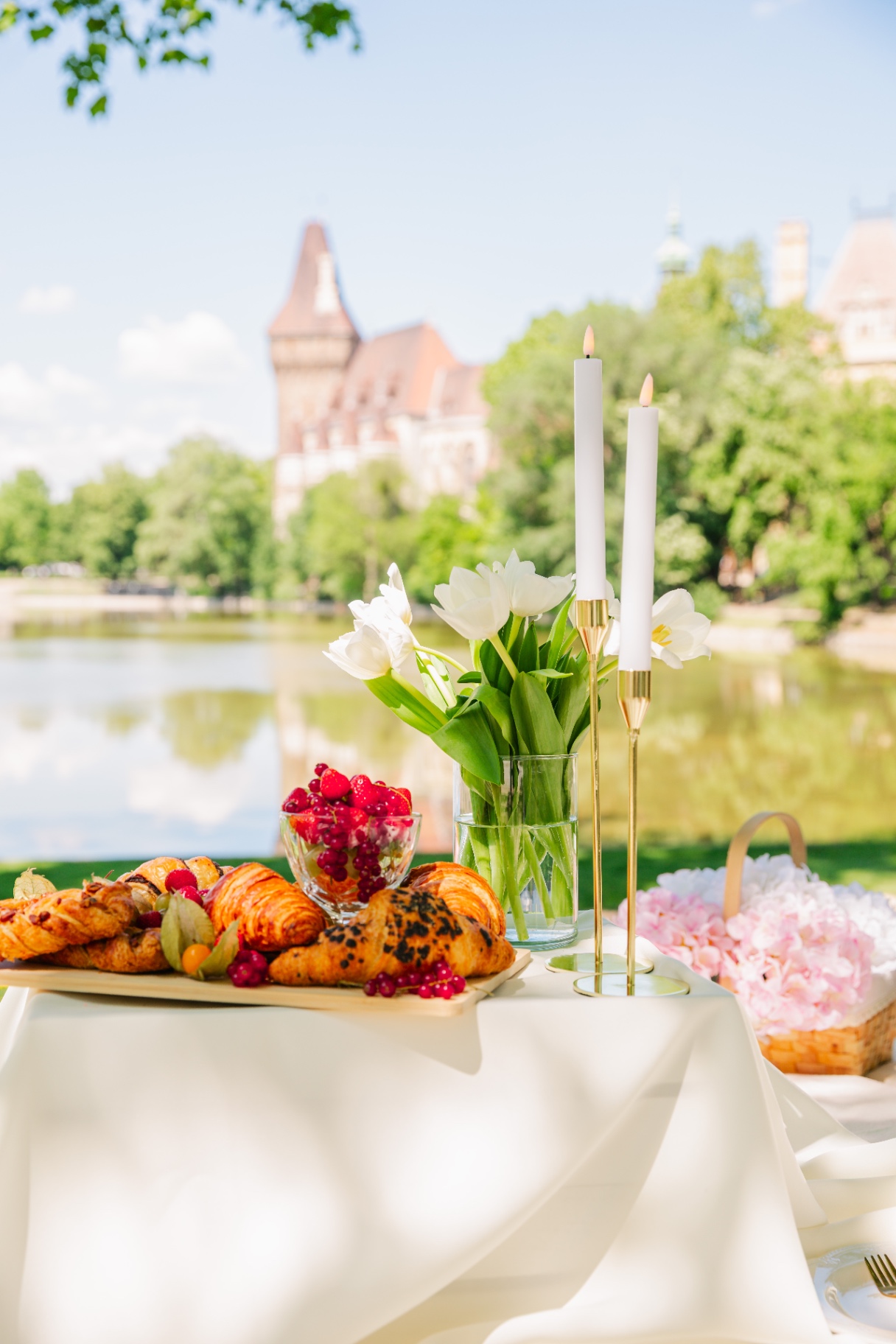 Luxury picnic setup with Vajdahunyad Castle backdrop, pastries, berries and white tulips — Vivielle Events Budapest