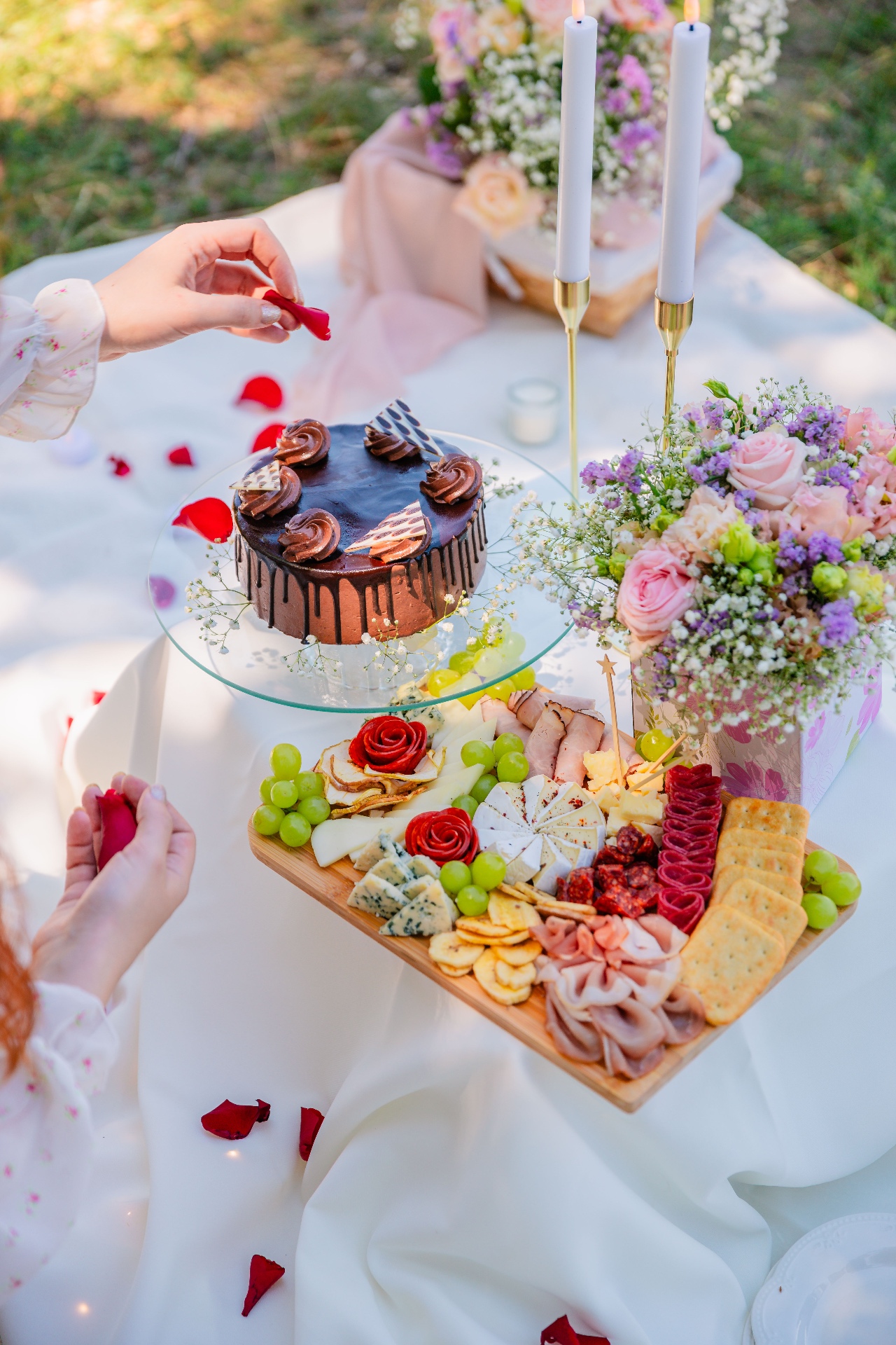 Luxury proposal picnic in Budapest with chocolate drip cake, gourmet charcuterie board and pastel florals with rose petals by Vivielle Events